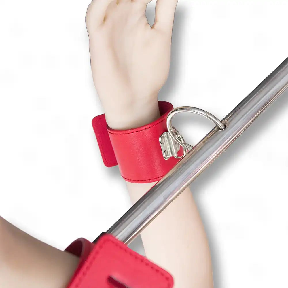 Barre d'écartement en acier avec menottes rouges portées aux poignets, accessoire de soumission et de bondage pour adultes.