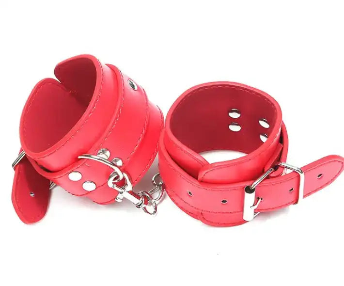 Menottes en cuir rouge vif reliées par une chaîne en acier, accessoire de soumission et sissy pour adultes.