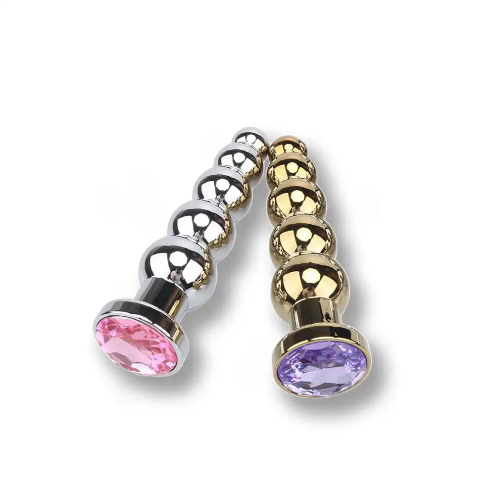 Gros plan sur les bases serties de strass rose et violet des plugs anaux en métal, bijoux anaux et accessoires de sissification.